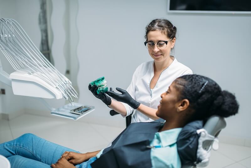 dentist-shows-dentures-to-woman-in-a-dental-chair-4ERHV5T